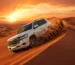 Desert sand bashing Dubai SUV climbing golden dunes at sunset