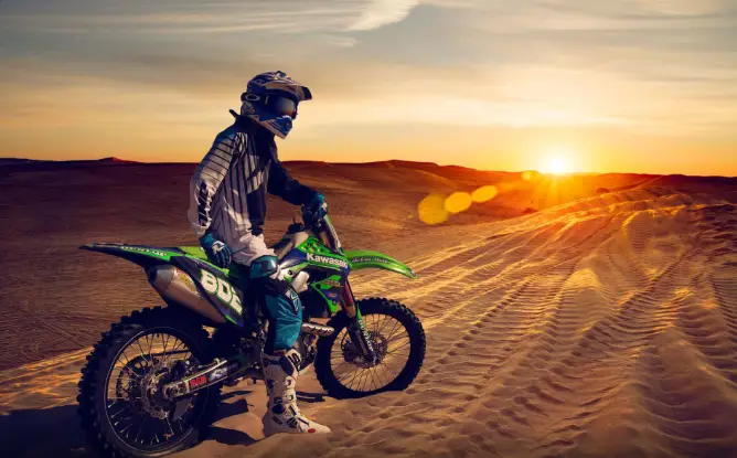Dirt bike rental Dubai rider jumping over red sand dunes at sunset